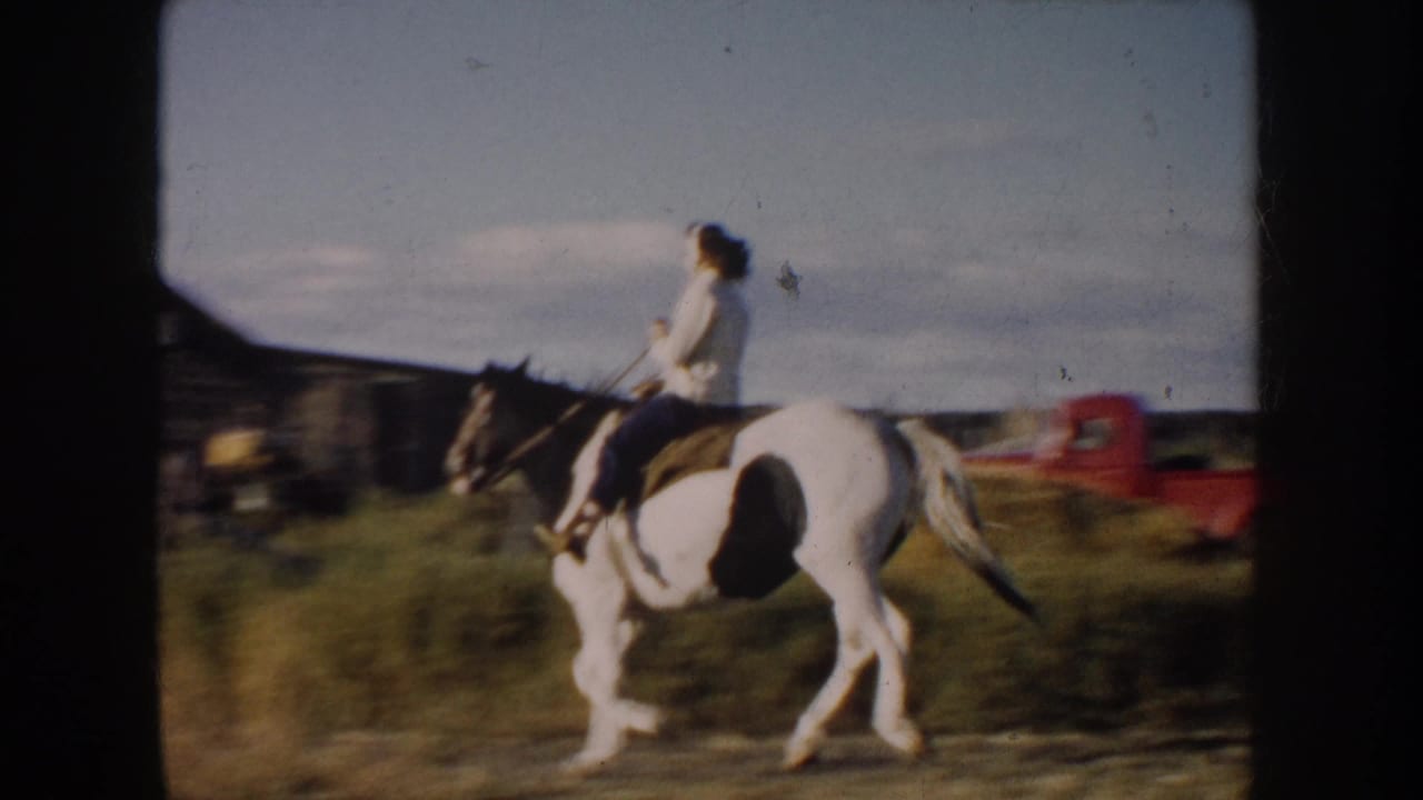 Mounted rider passing near wooden structures with red farm equipment in the background.