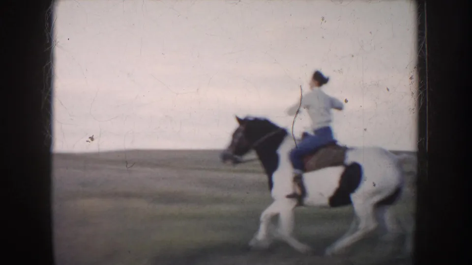 1953 South Dakota 8mm frame with a rear view of a rider on a pinto horse moving through an open field.