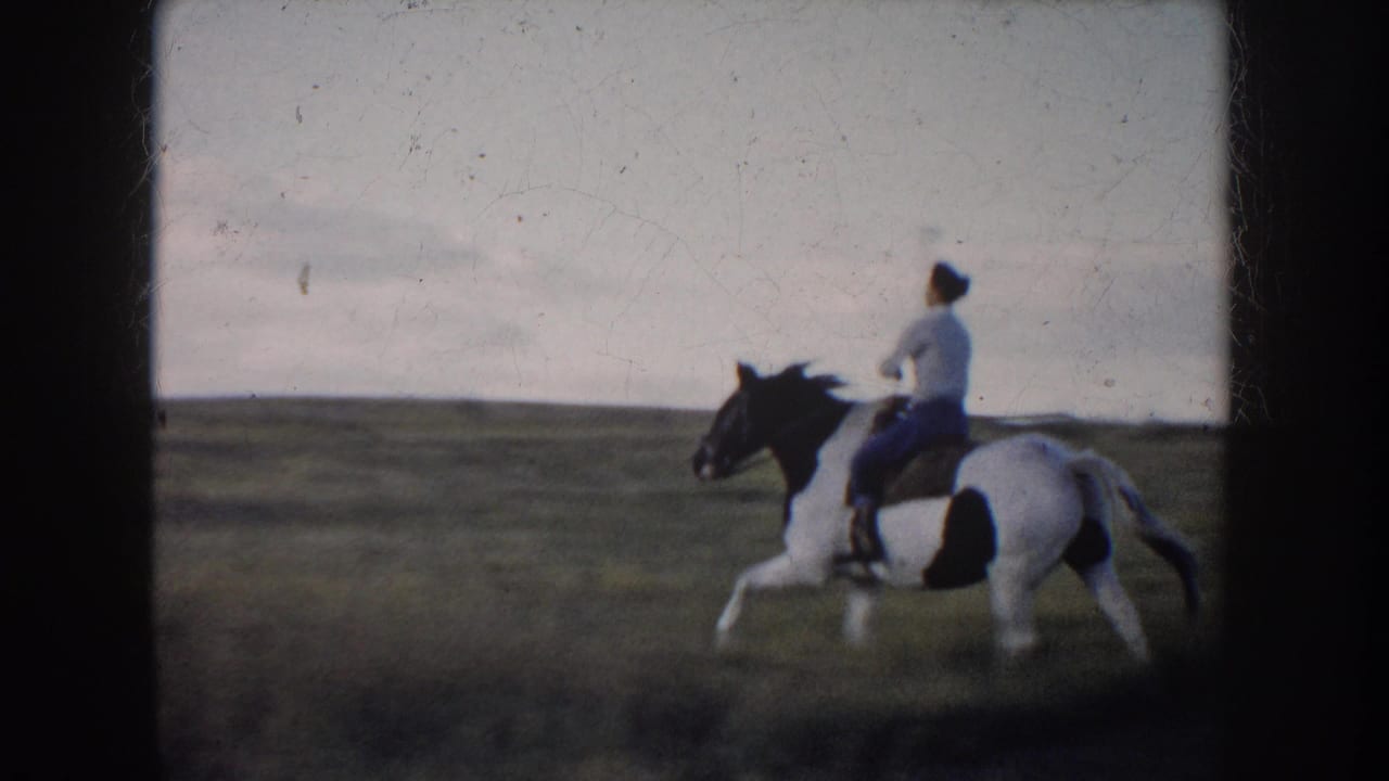 1953 South Dakota 8mm frame showing a rider on a pinto horse galloping through a broad rural field.