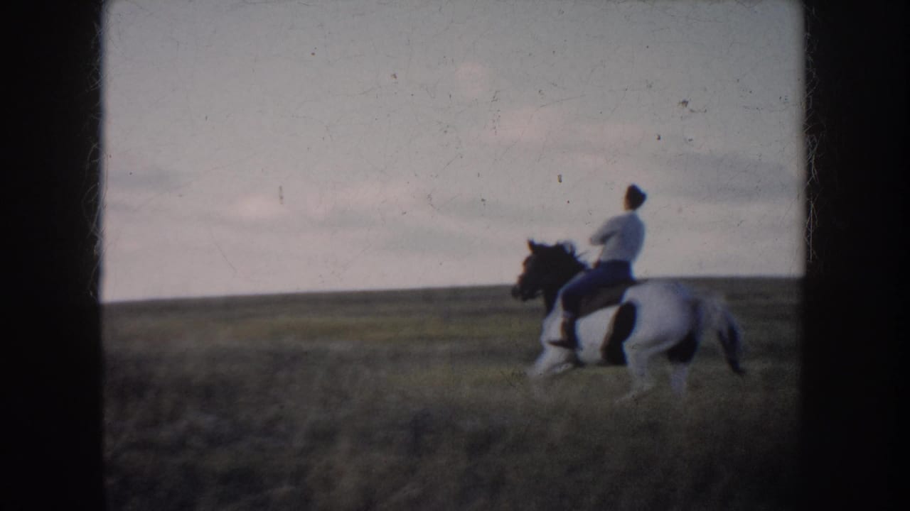1953 South Dakota home-movie frame showing a man on a black-and-white horse in open grassland under a cloudy sky.