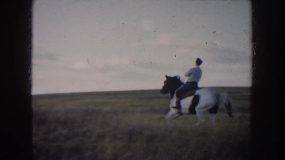 1953 South Dakota home-movie frame showing a man on a black-and-white horse in open grassland under a cloudy sky.