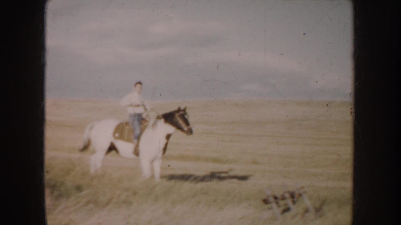 A man on a pinto horse appears in open South Dakota grassland, with small farm equipment visible near the frame edge.