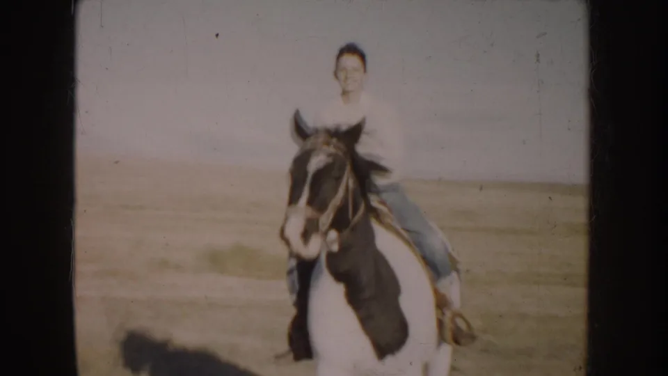 A front-facing view shows the young rider smiling while mounted on the pinto horse in the rural South Dakota field.