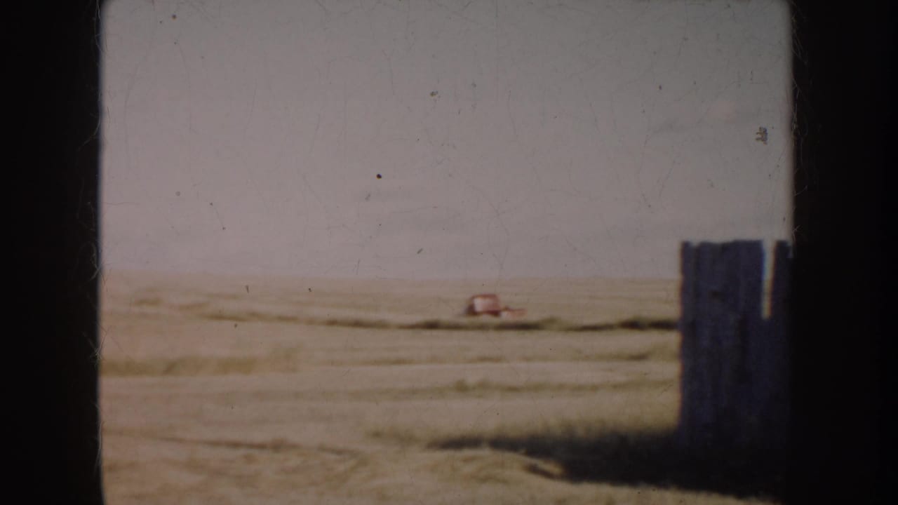 1953 South Dakota prairie view on 8mm film, with a small red pickup in the distance and a dark post or fence element at right.