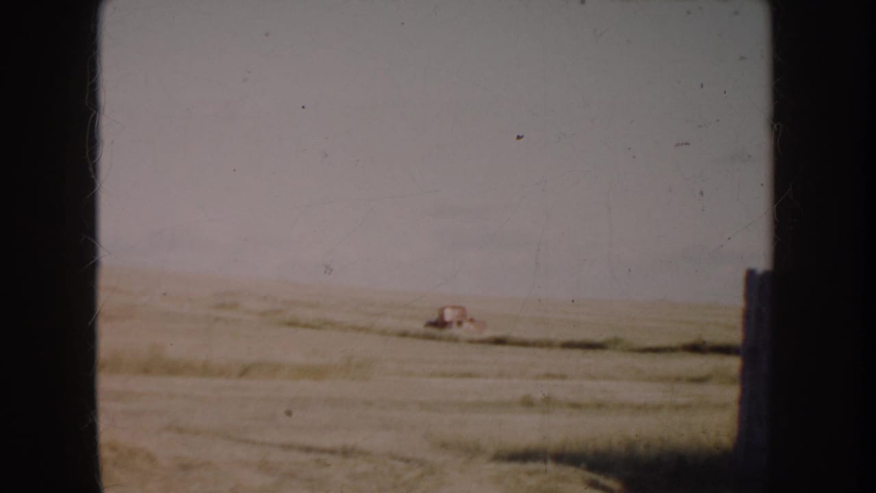 1953 South Dakota home-movie frame showing a red pickup far across a flat prairie field, with soft focus and visible film borders.