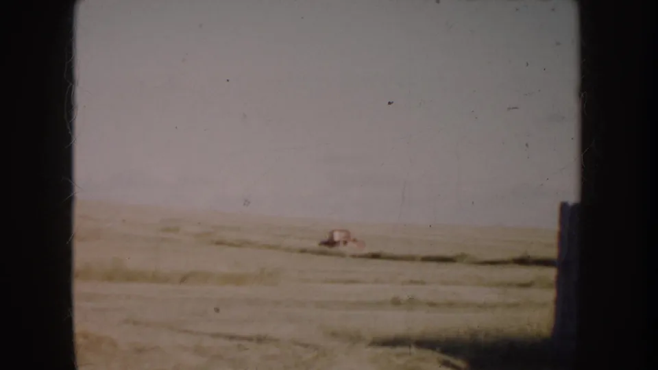 1953 South Dakota home-movie frame showing a red pickup far across a flat prairie field, with soft focus and visible film borders.