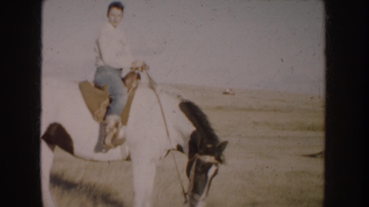 1953 South Dakota home-movie frame showing a woman seated on a white horse, facing the camera across sunlit prairie land.