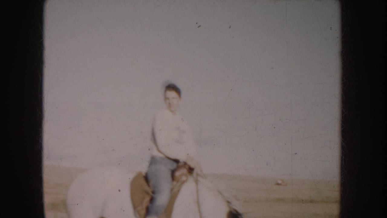 1953 South Dakota 8mm frame showing a woman on horseback in a wide grassy field under a pale sky.