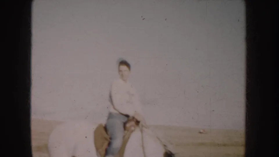 1953 South Dakota 8mm frame showing a woman on horseback in a wide grassy field under a pale sky.