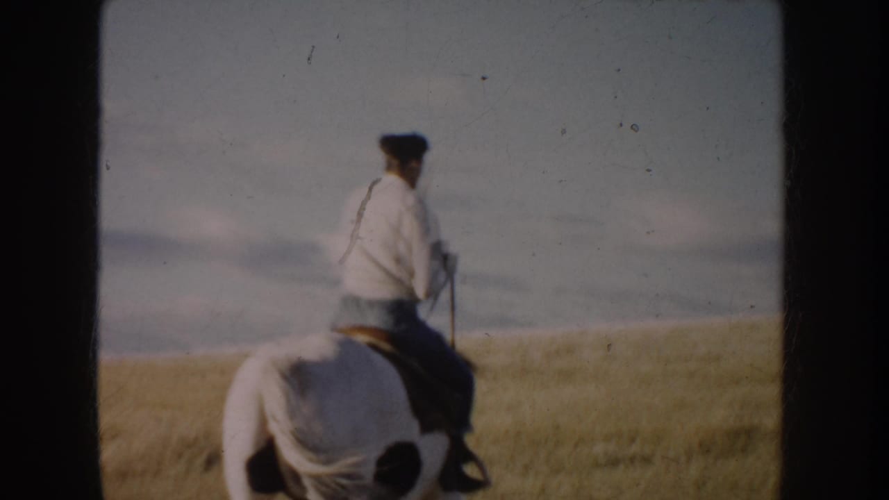 Rear view of a woman riding a dark brown and white horse through South Dakota grassland in 1953 home-movie footage.