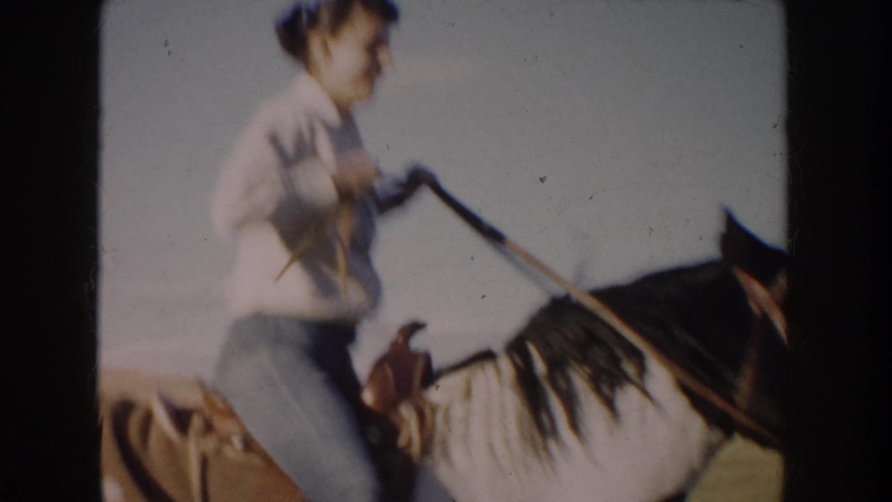 Close 8mm view of the woman rider holding the reins as the horse passes through the open South Dakota field.