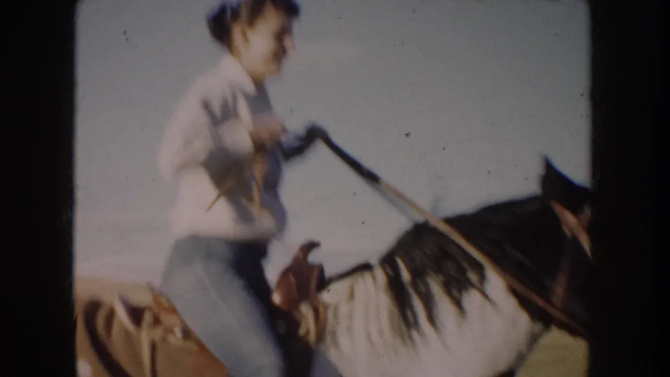Close 8mm view of the woman rider holding the reins as the horse passes through the open South Dakota field.
