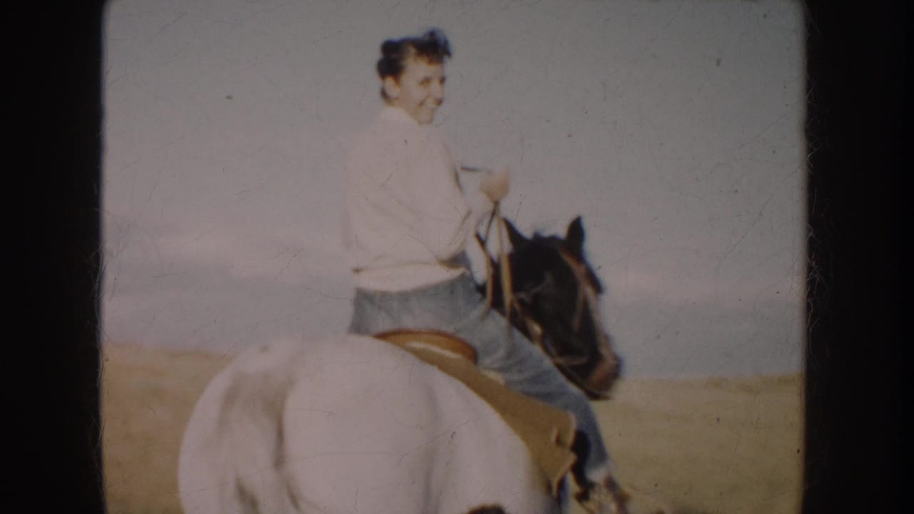 Woman on horseback looks toward the camera in a 1953 South Dakota home-movie frame, with grassland and sky behind her.