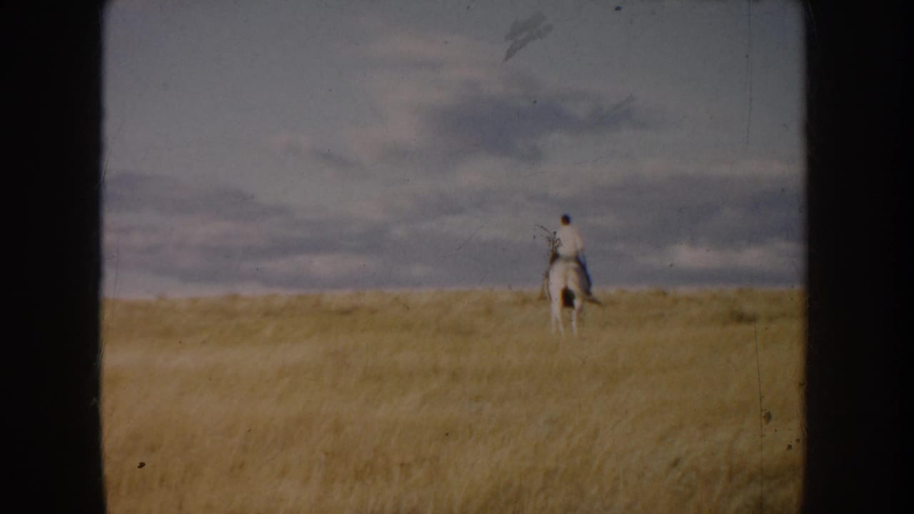 1953 South Dakota 8mm frame showing a lone rider on a white horse crossing open golden prairie under layered clouds.