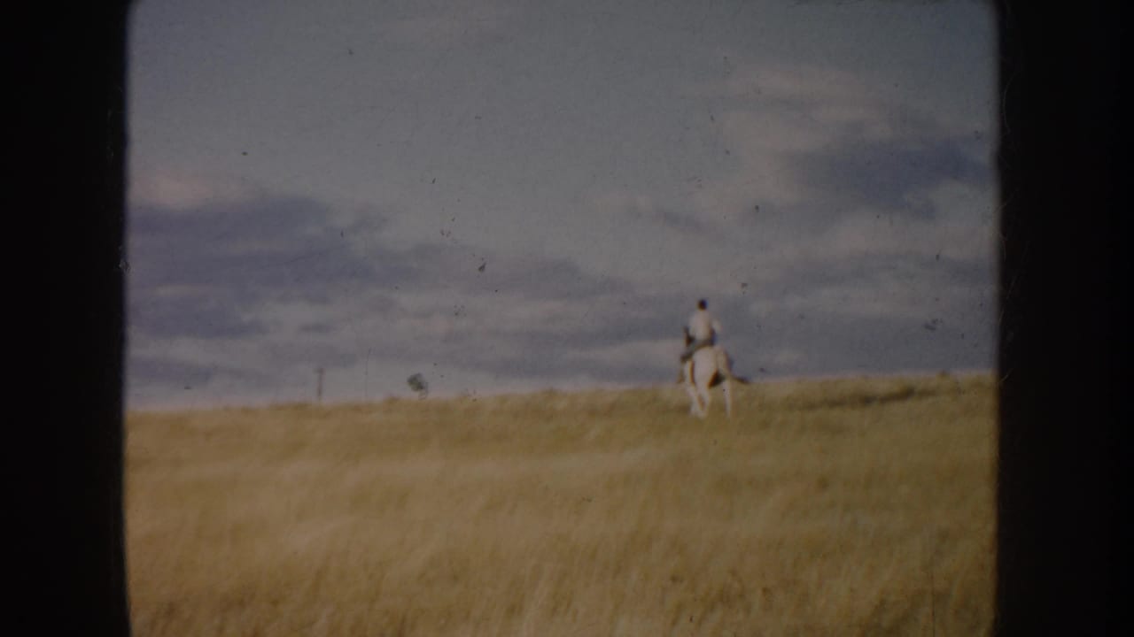 A lone horseback rider appears near the horizon on open South Dakota prairie, framed by golden grass and a cloudy 1950s 8mm sky.