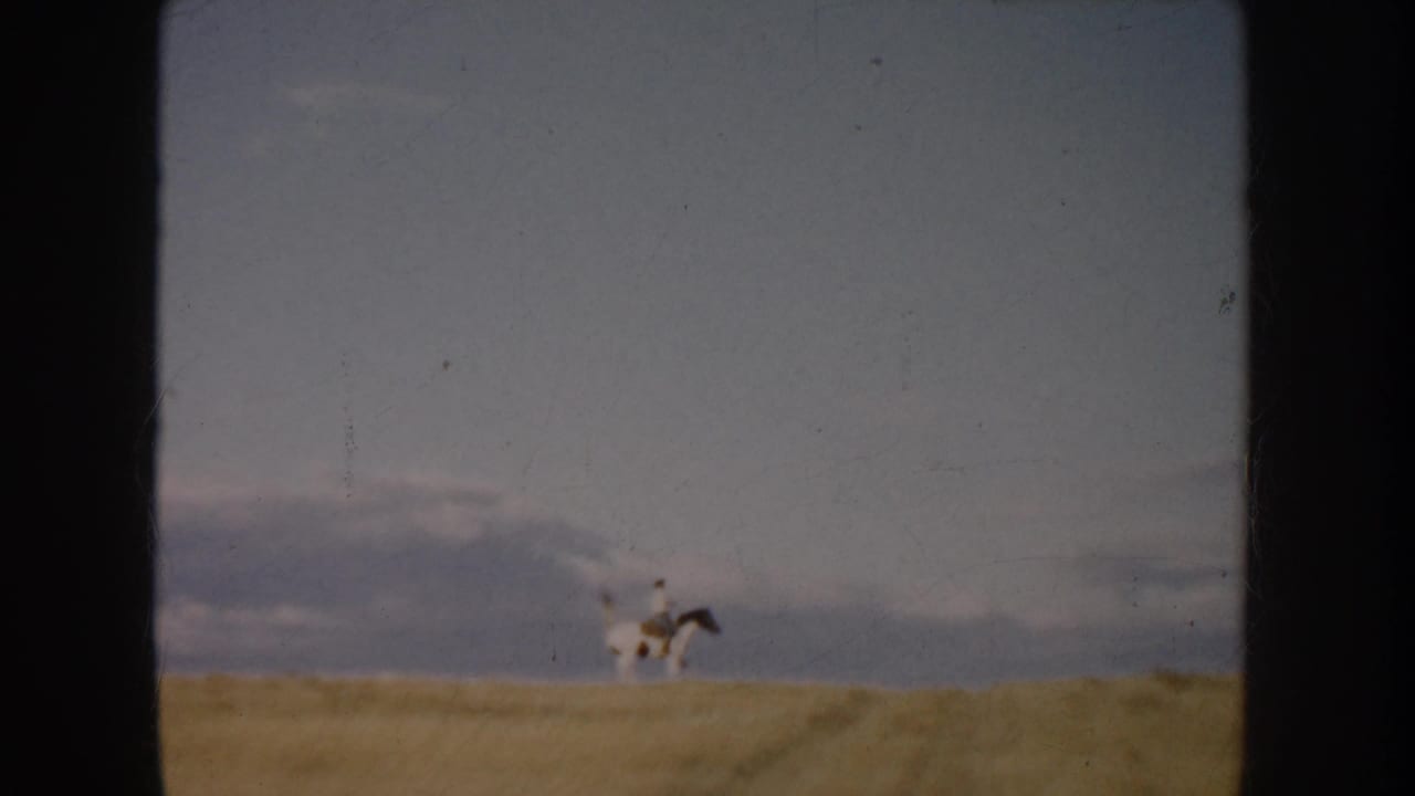 A distant horseback rider crosses the field horizon, with muted 8mm color and visible film wear from the 1953 South Dakota reel.