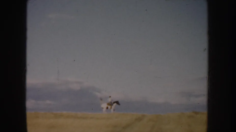 A distant horseback rider crosses the field horizon, with muted 8mm color and visible film wear from the 1953 South Dakota reel.