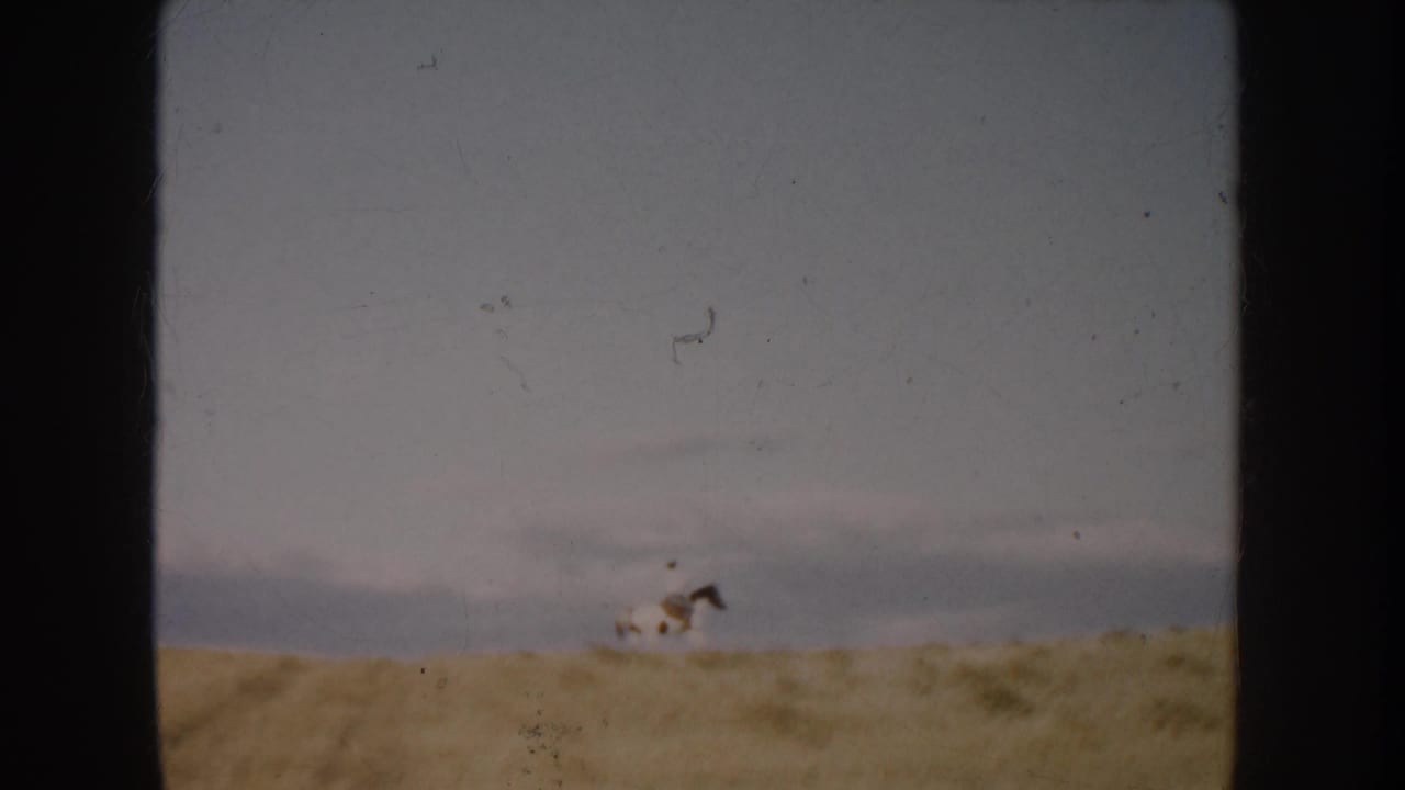 1953 South Dakota 8mm frame with a distant rider on a spotted horse moving across an open dusty field.