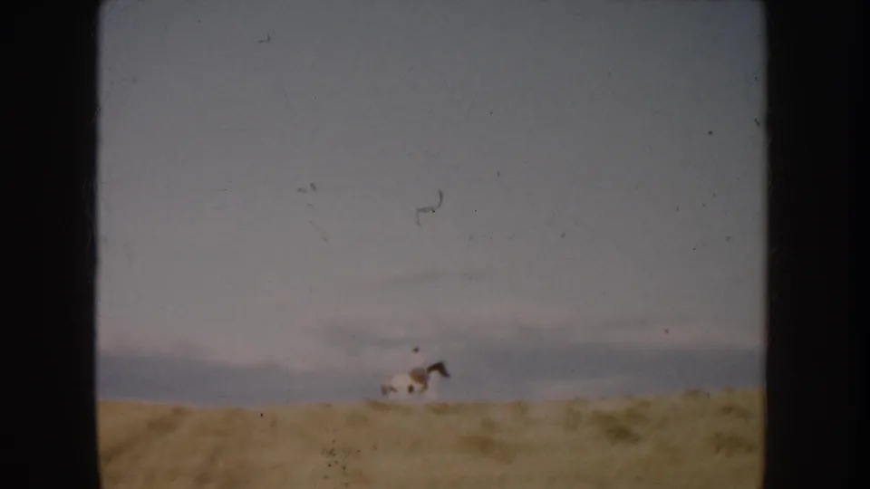 1953 South Dakota 8mm frame with a distant rider on a spotted horse moving across an open dusty field.