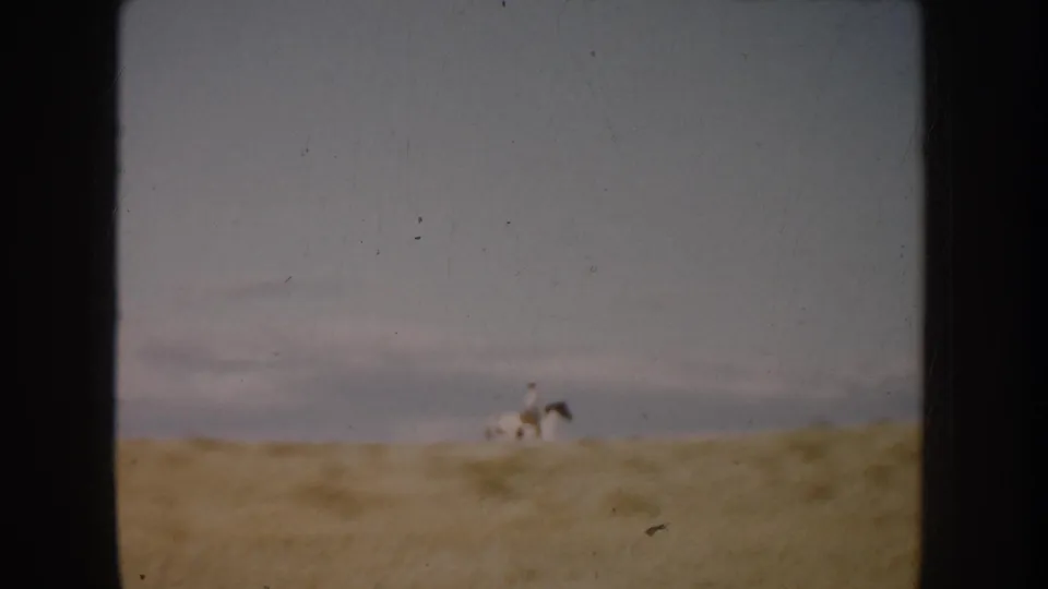 A distant rider on a spotted horse crosses a South Dakota field in faded 1950s home-movie footage.
