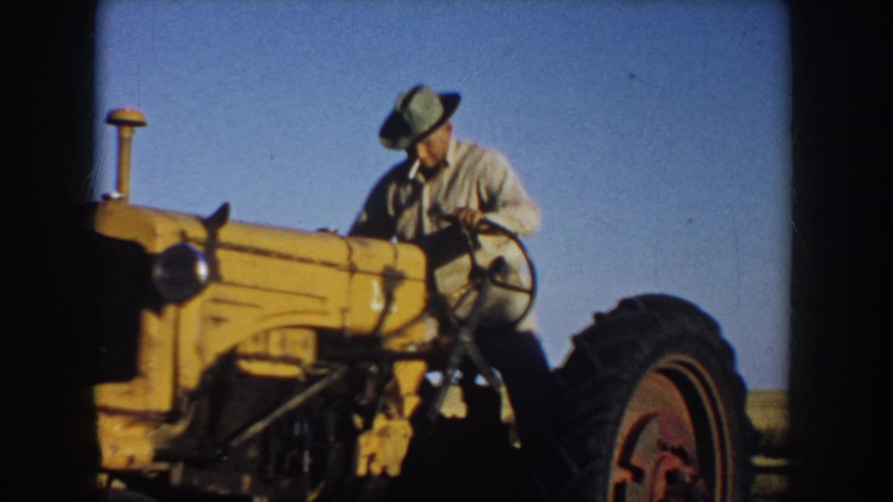 A 1953 South Dakota home-movie frame shows the farmer looking down at the tractor controls while seated or climbing onto the yellow tractor.