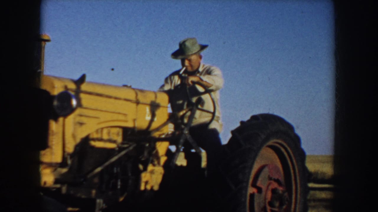 1953 South Dakota farm footage showing a man at the controls of a yellow tractor under a clear sky.