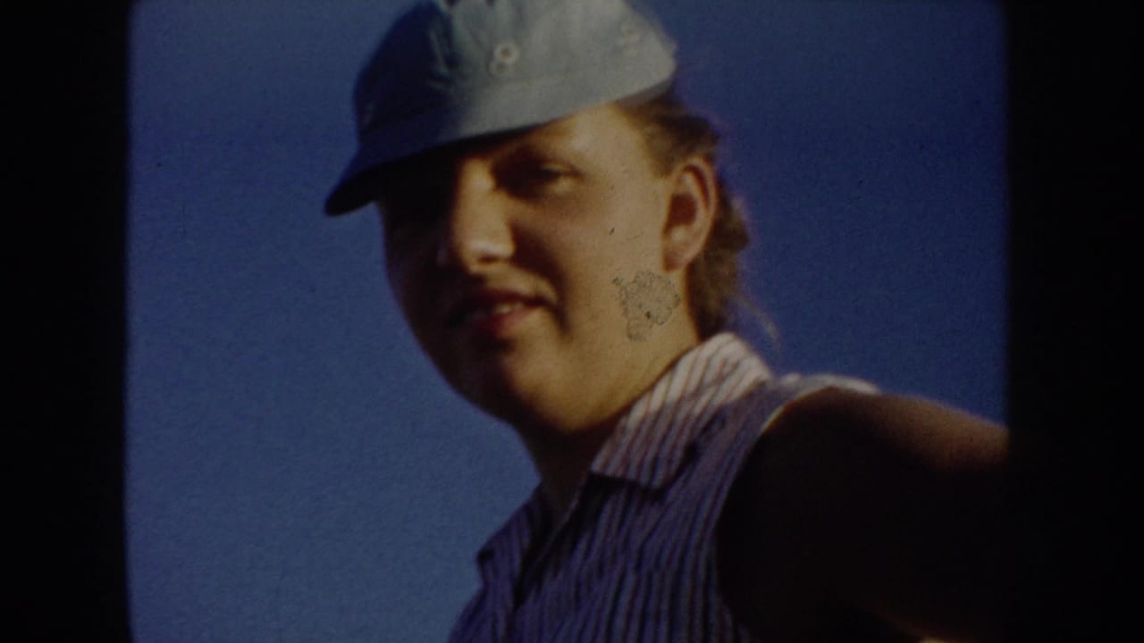 Close home-movie portrait of a young woman or teen in a blue cap and striped sleeveless shirt against the South Dakota sky.