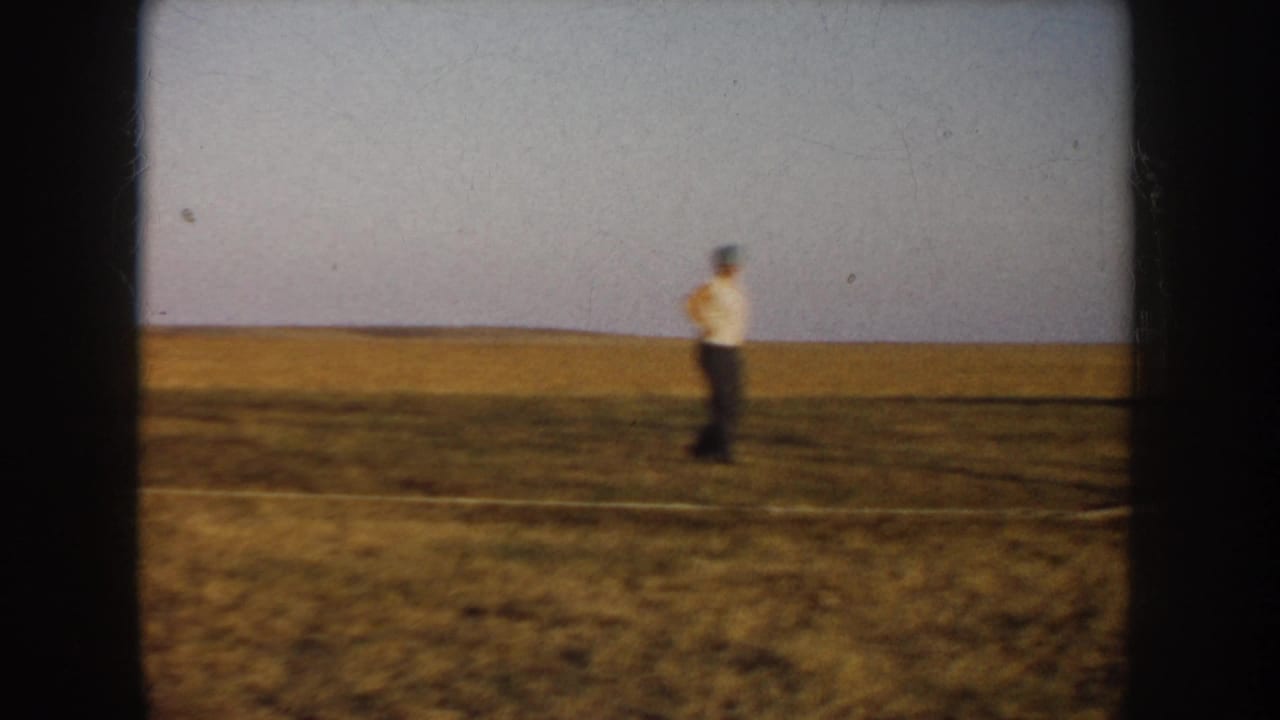 Distant man in a white shirt and dark pants crossing an open South Dakota farm field in 1953 home-movie footage.