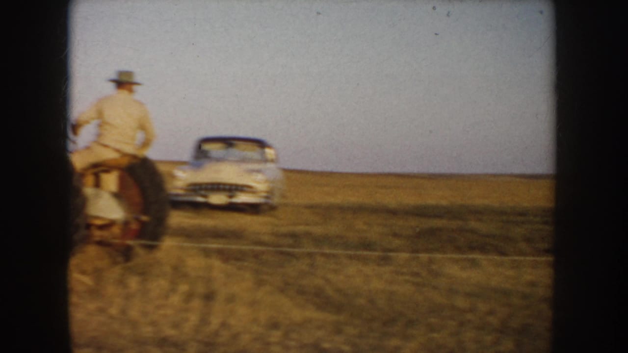 1953 South Dakota home-movie frame showing a tractor driver near a parked period car on an open prairie field.