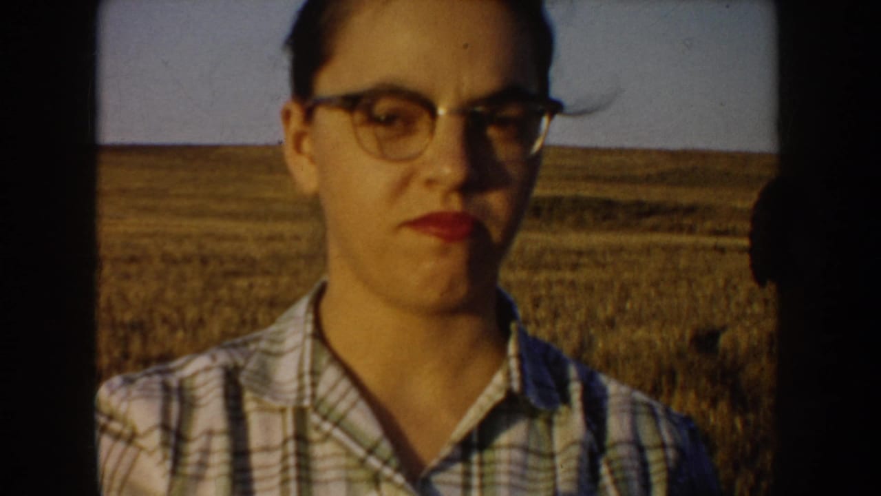 Woman in glasses and plaid shirt standing before a flat prairie field.