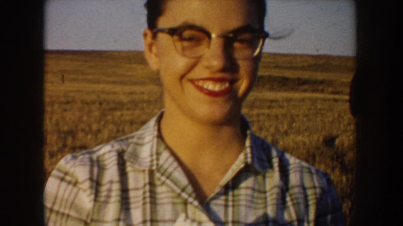 Smiling woman in glasses stands close to the camera in South Dakota prairie home-movie footage from 1953.