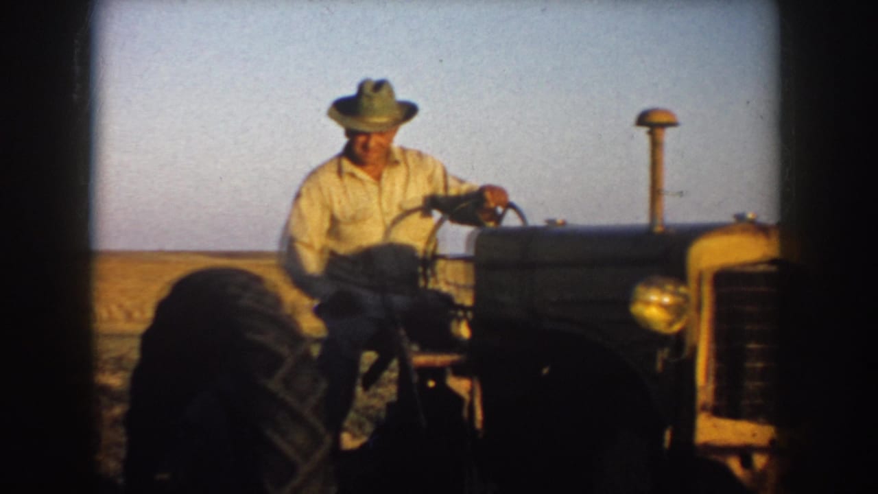 Farmer seated on a tractor with the steering wheel and exhaust stack visible.
