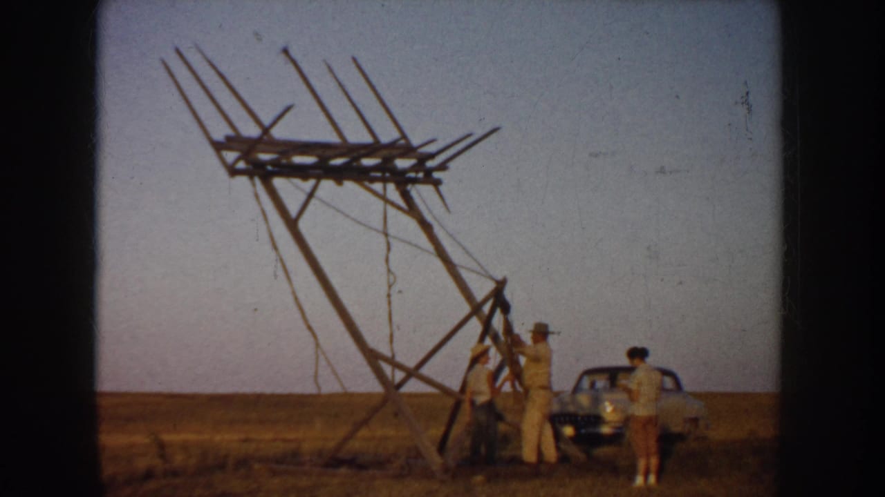 South Dakota 1953 home-movie footage shows men clustered under a tall wooden antenna-like frame, with a parked car at right.
