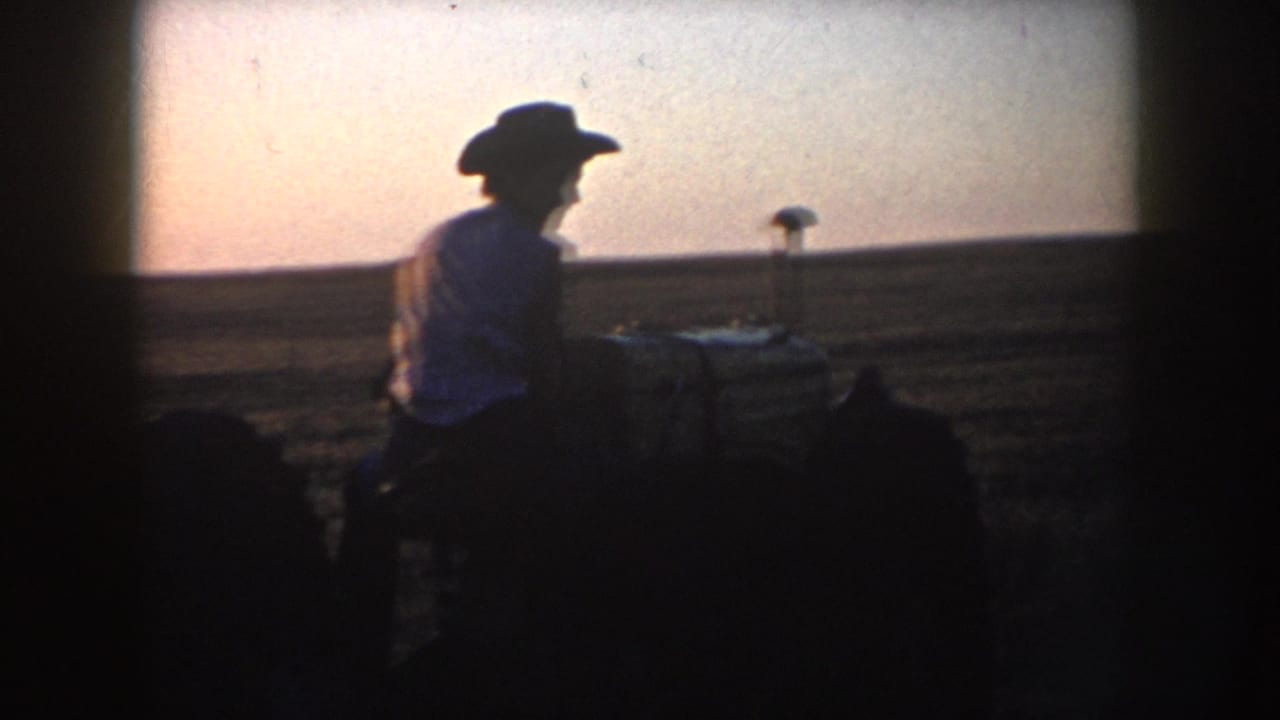Man in a cowboy hat sits on or operates a tractor silhouetted against a low sky.