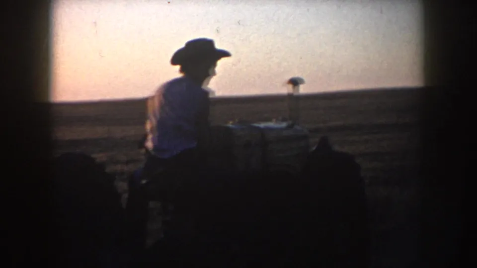 A man in a cowboy hat appears on a tractor in a South Dakota field, silhouetted by the fading 1953 evening light.