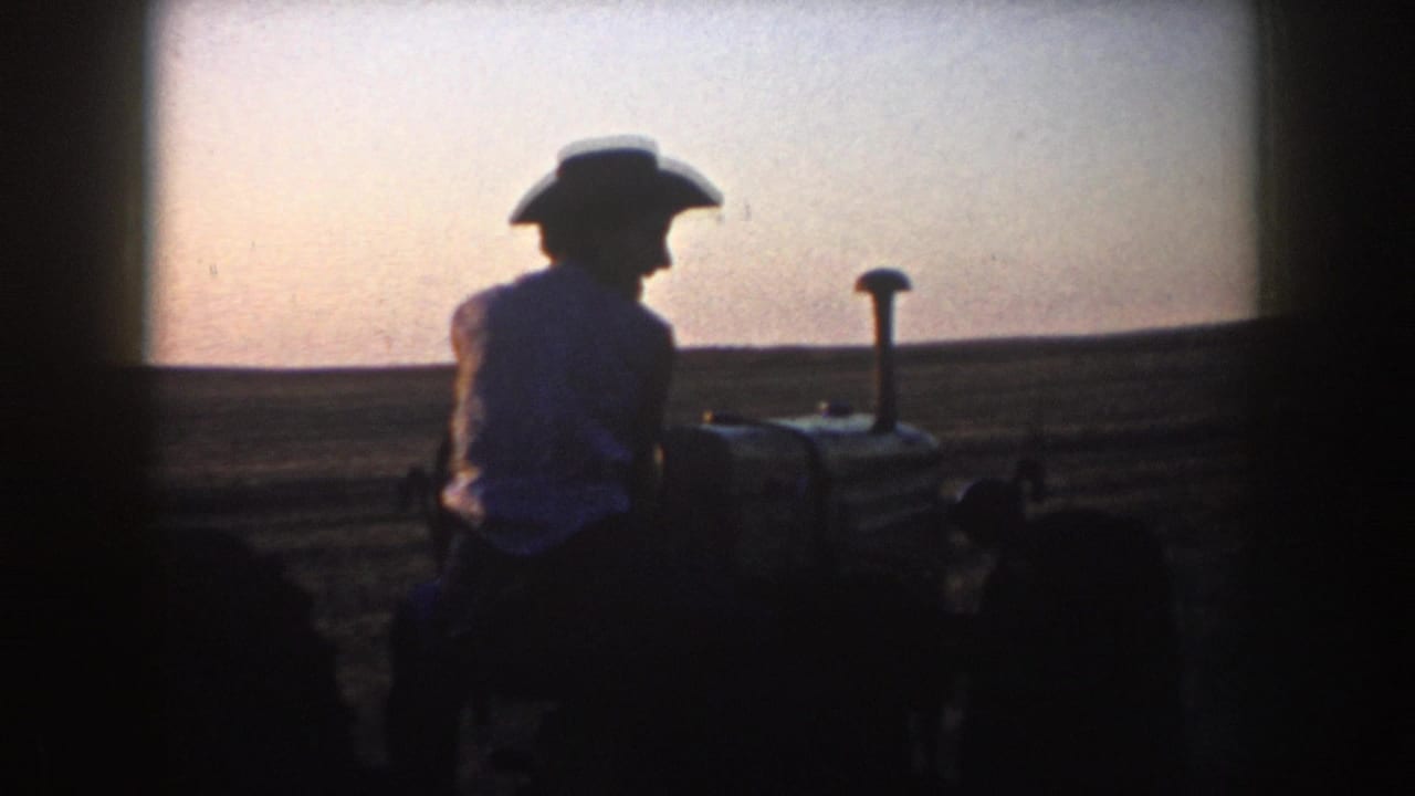 Backlit 1953 South Dakota farm footage shows a man in a cowboy hat seated on a tractor against a pale evening sky.