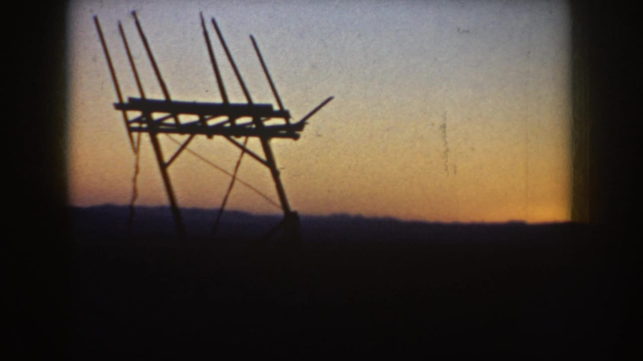 1953 South Dakota 8mm frame of a television antenna silhouette with multiple rods, dark horizon, and warm evening sky.