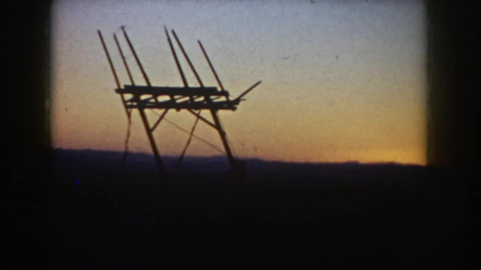1953 South Dakota home-movie frame with a dark rural antenna-like structure in front of a pale sunset gradient.