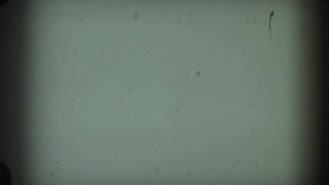A mostly blank 8mm frame with pale green exposure, dark vertical edge shading, and visible dust or film marks.