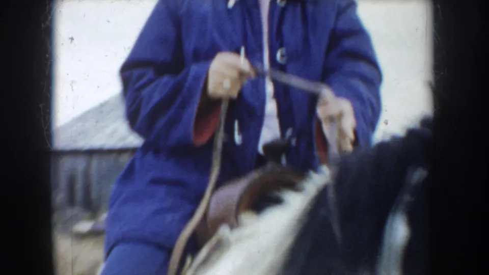The home-movie frame closely crops the South Dakota rider's blue jacket, hands, reins, saddle, and part of the pinto horse.