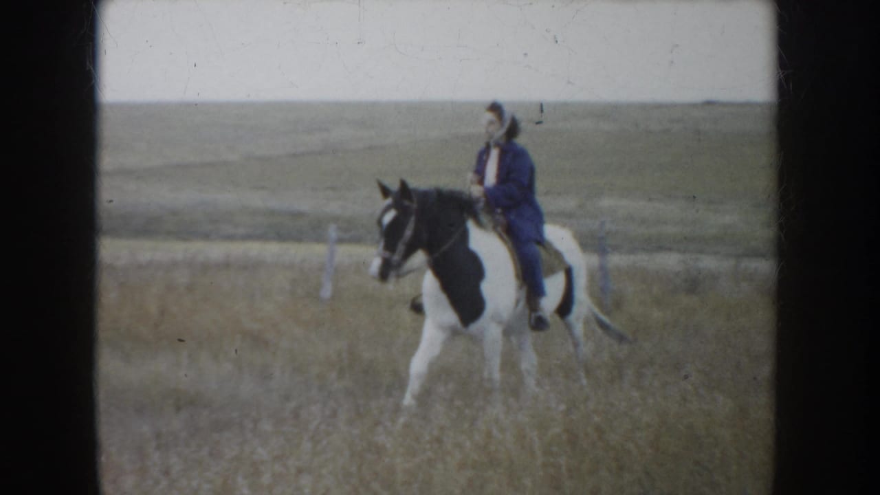 1953 South Dakota frame showing a rider in a dark jacket and hat on a black-and-white horse among dry prairie grass.