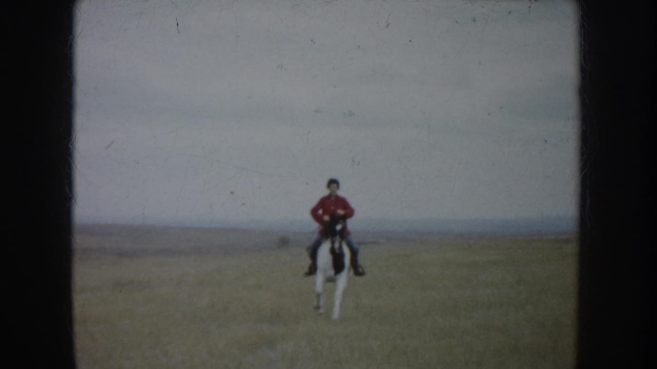 In 1953 South Dakota footage, a rider in a red shirt approaches across an open field on a white-and-dark horse.