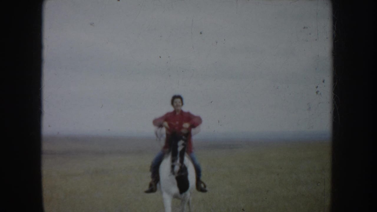 A rider in red and blue jeans faces the camera on horseback in the South Dakota home-movie scene.