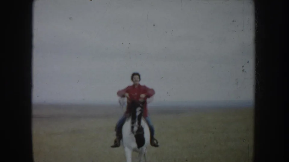 A rider in red and blue jeans faces the camera on horseback in the South Dakota home-movie scene.