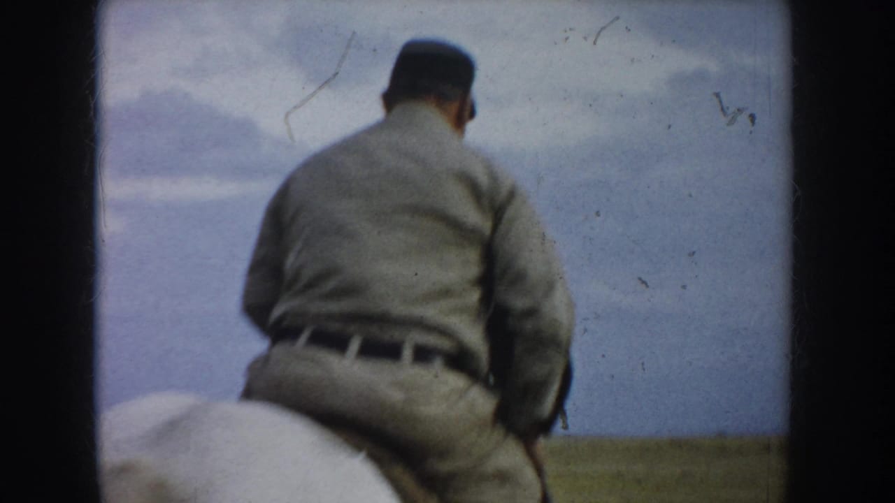 In 1953 South Dakota home-movie footage, a man in light uniform-style clothing rides a spotted horse away across prairie grass.