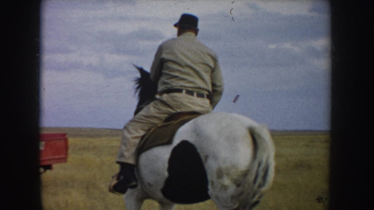 The rider continues away on the spotted horse, with prairie grass, cloudy sky, and a partial red vehicle or trailer visible at left.