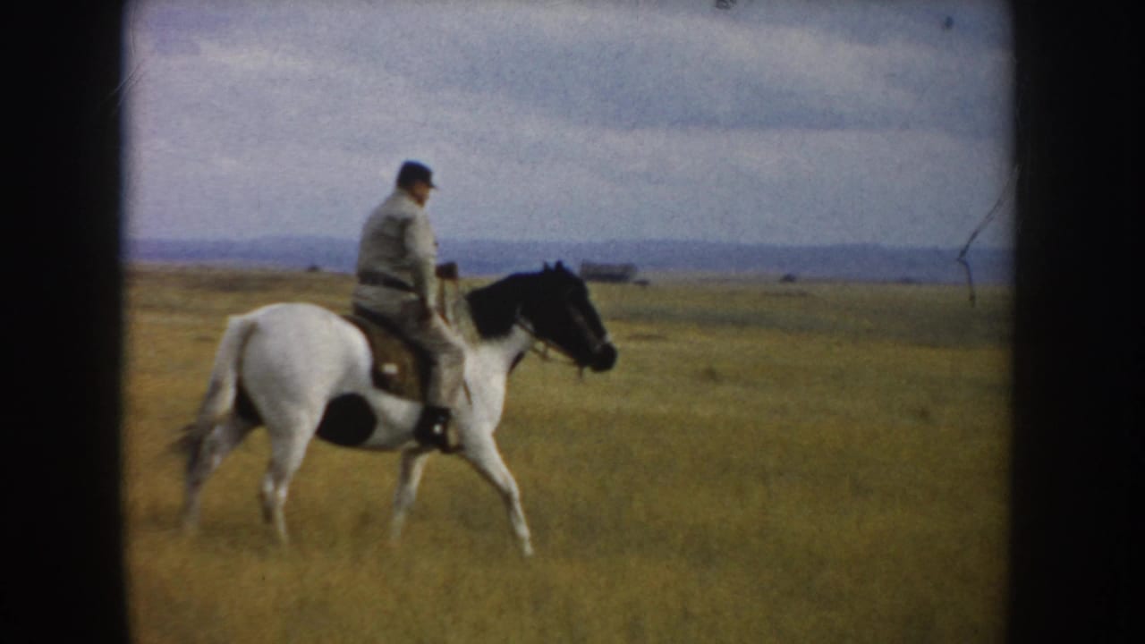 Adult rider on a white-and-black horse crosses open South Dakota grassland with a distant low horizon behind them.