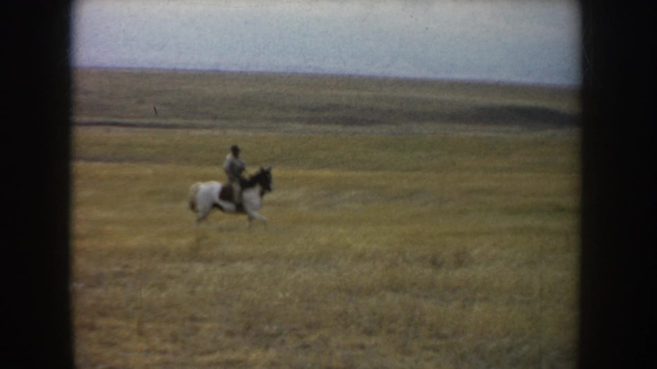 The clip ends with the rider and white horse with dark markings continuing across the open South Dakota prairie landscape.