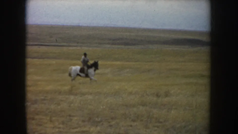 The clip ends with the rider and white horse with dark markings continuing across the open South Dakota prairie landscape.
