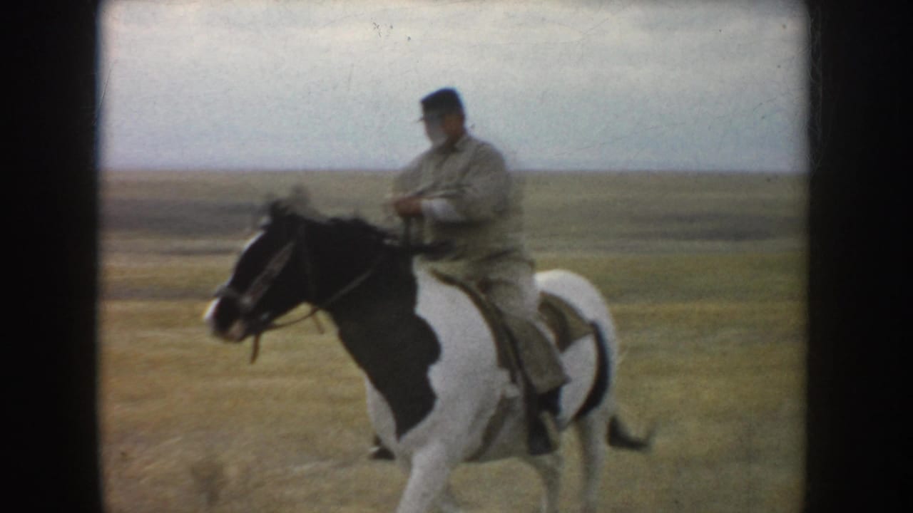 The adult rider turns the pinto horse sideways in the open South Dakota field, with flat prairie and pale sky behind them.